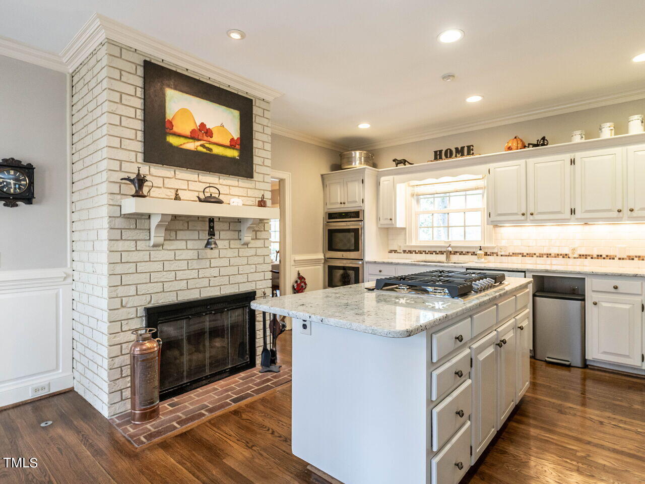 Kitchen with a granite cooktop island and white brick fireplace.