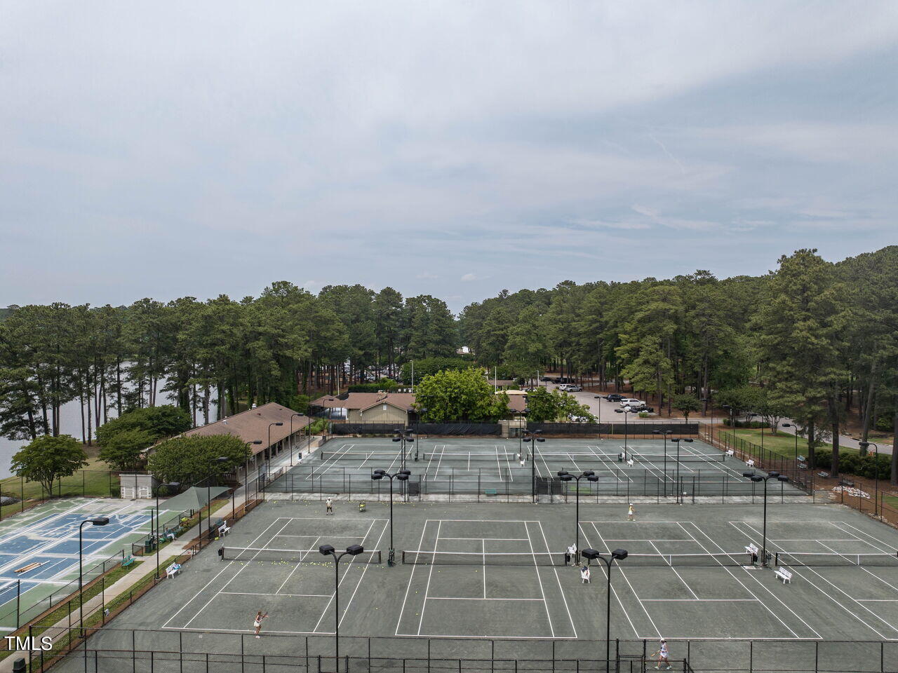 Aerial view of outdoor tennis courts beside a wooded lake.