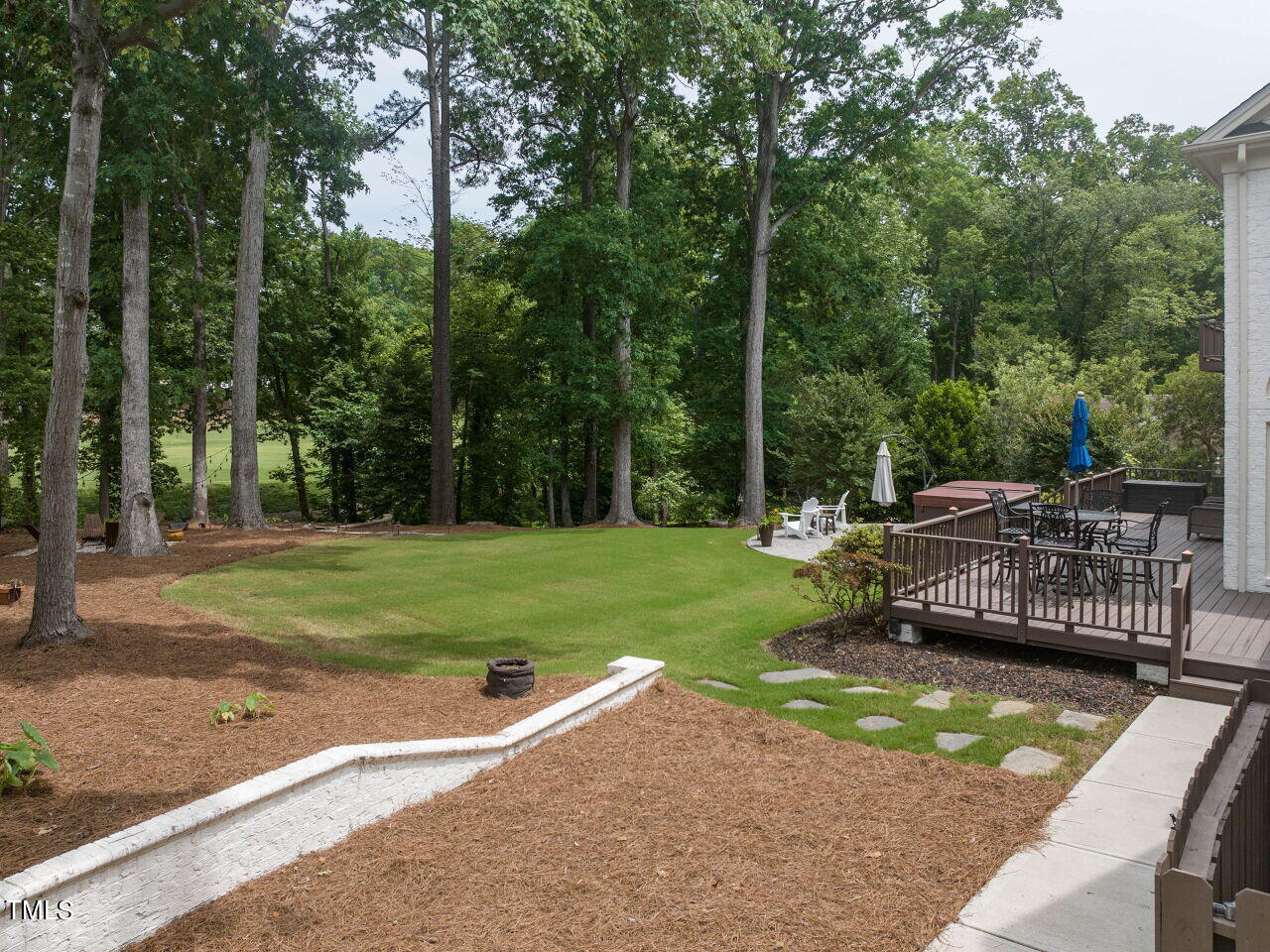 Backyard with a grassy lawn, wooded border, and raised deck furnished for outdoor dining.