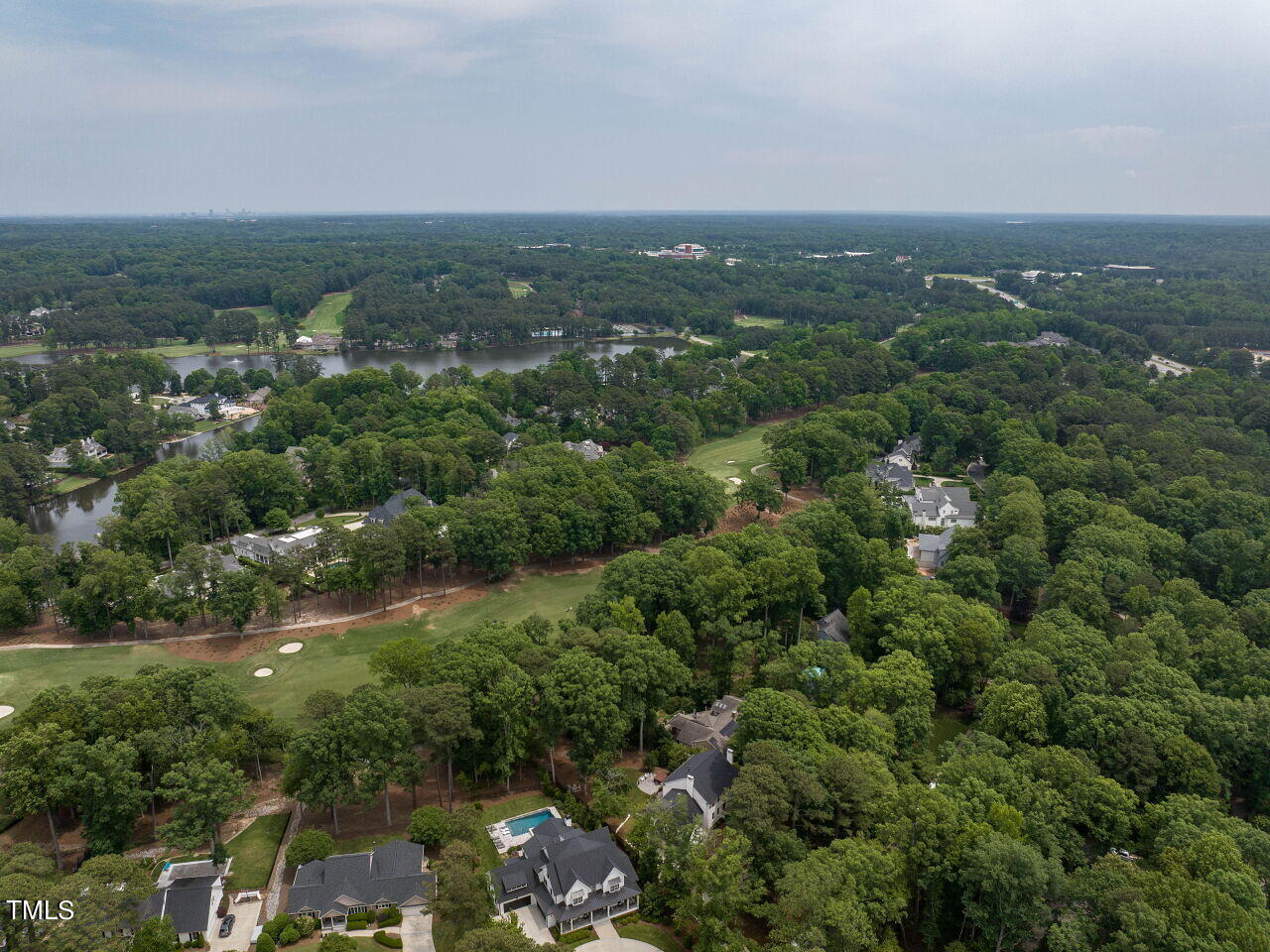 Aerial view of a wooded neighborhood with a lake and golf course.
