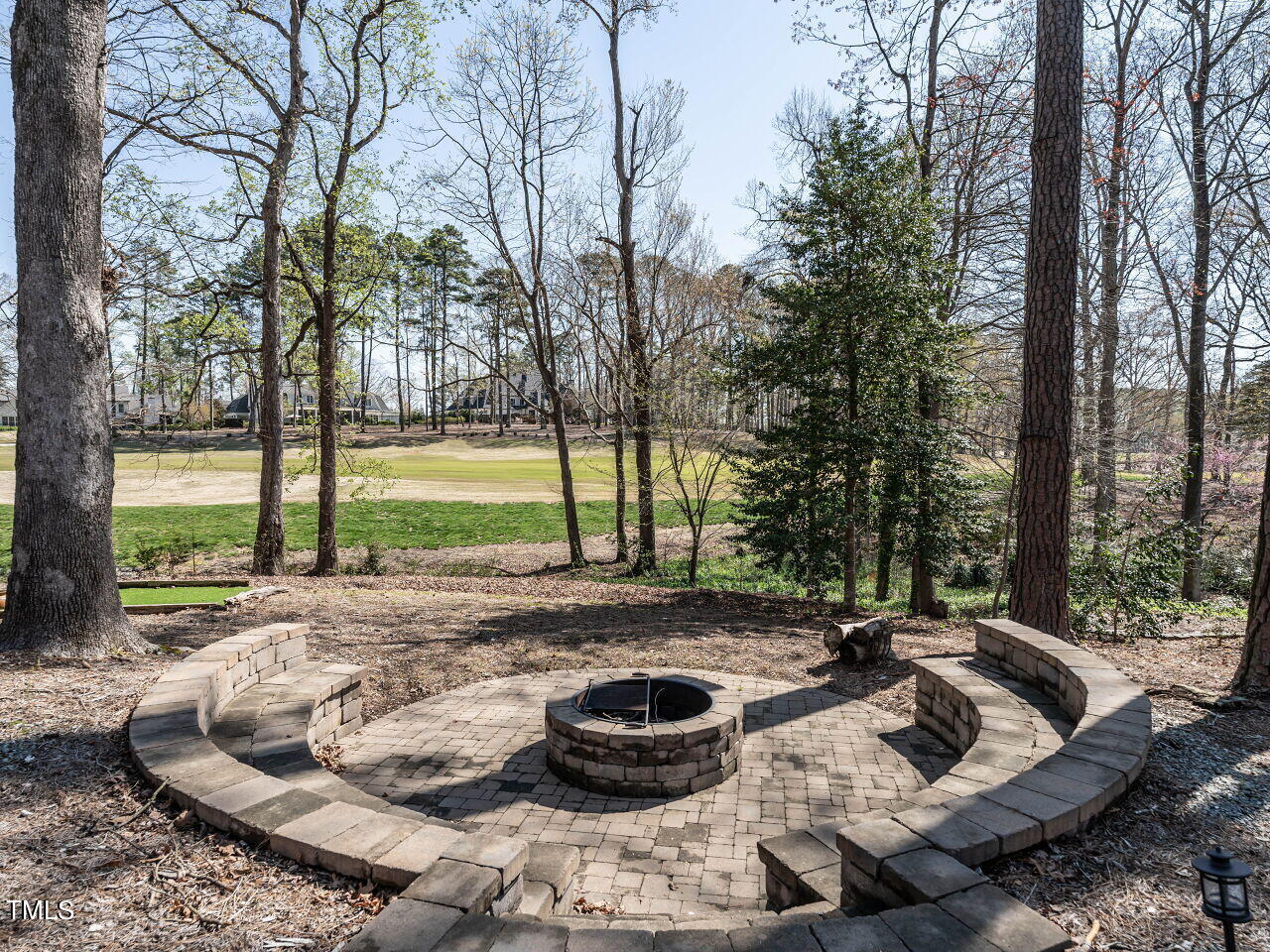 Backyard patio with a circular stone fire pit and built-in seating overlooking a golf course.