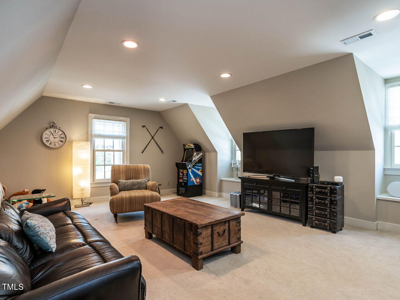 Upstairs living room with a sloped ceiling, leather sofa, television, and arcade cabinet.