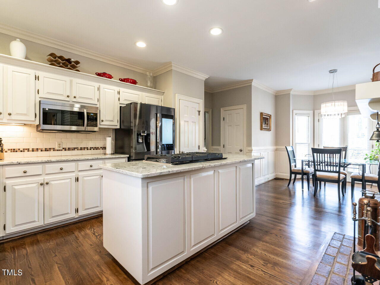 Kitchen with a large granite island, white cabinets, stainless steel appliances, and adjoining dining area.