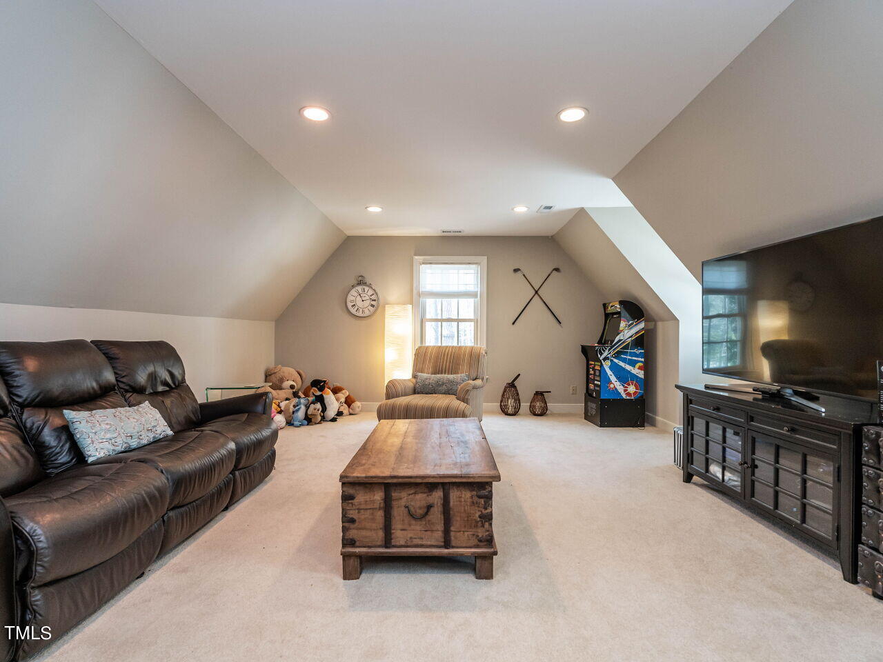 Upstairs bonus room with a leather sectional, wooden coffee table, and colorful arcade machine.