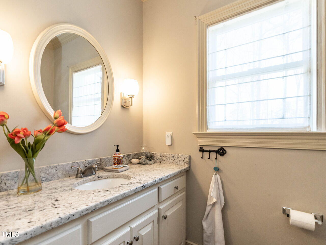 Bathroom vanity with a granite countertop, oval mirror, and large window.