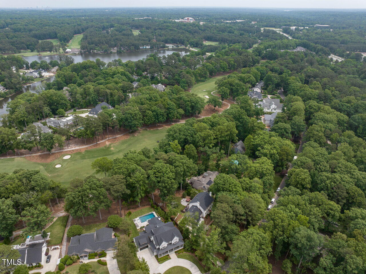 Aerial view of homes among trees beside a golf course and lake.