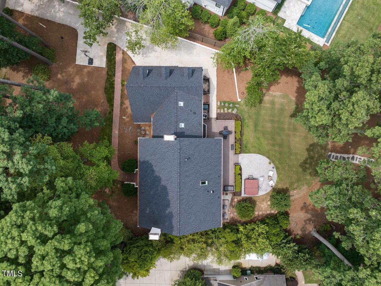 Aerial view of a home surrounded by mature trees, with a lawn and curved patio.