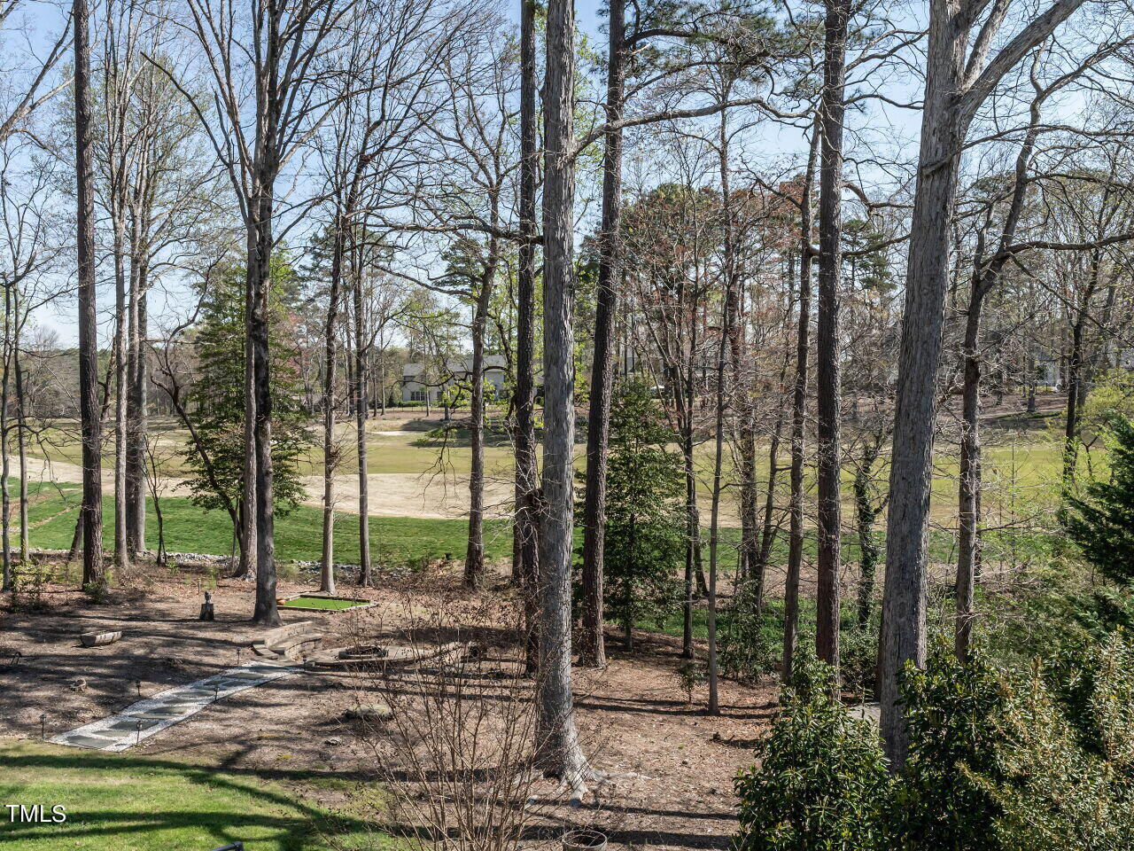 Wooded backyard overlooking a golf course, with a stone path and small putting green.