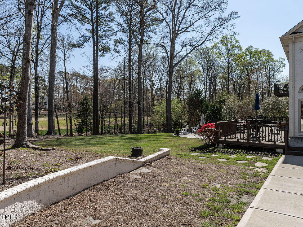 Backyard with a tree-lined view, grassy lawn, and furnished raised deck.