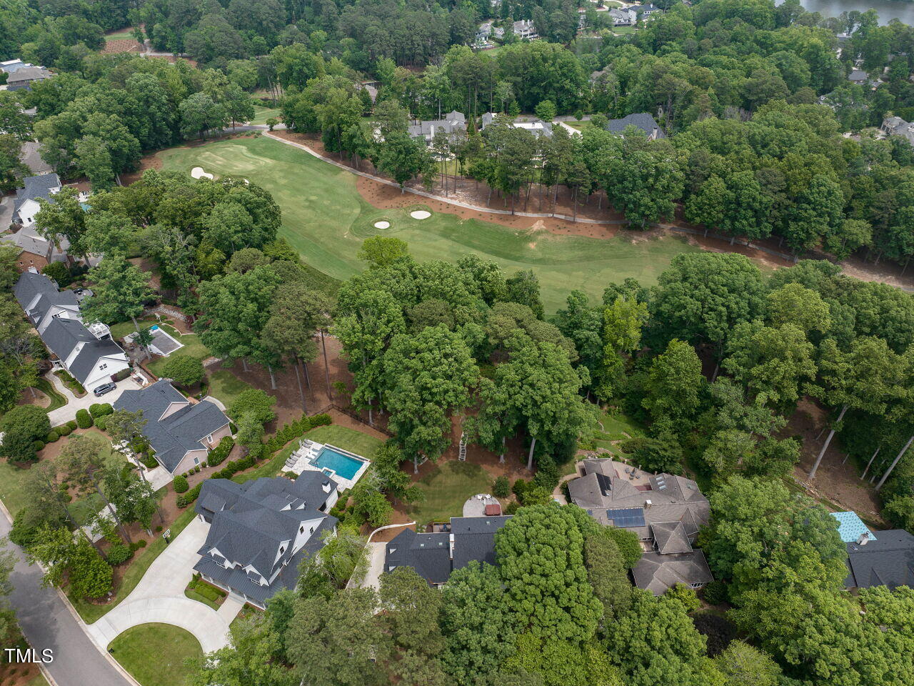 Aerial view of a golf course winding through a leafy neighborhood, with homes and swimming pools nearby.