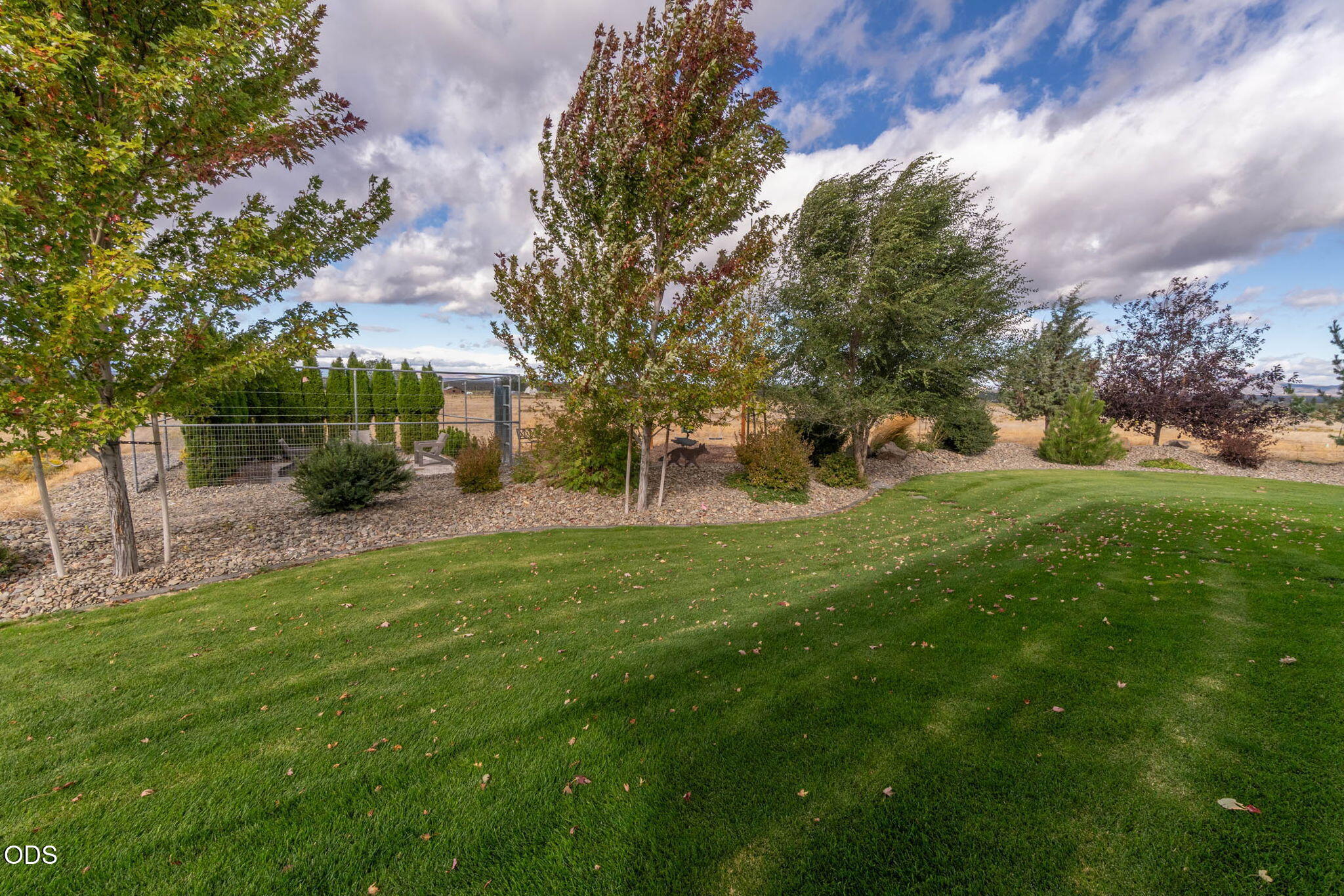 Landscaped backyard with a broad lawn, mature trees, and a fenced garden area.