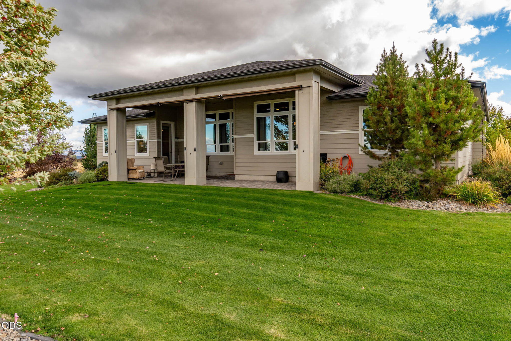 Home’s rear exterior with a covered patio, outdoor seating, and a broad green lawn.