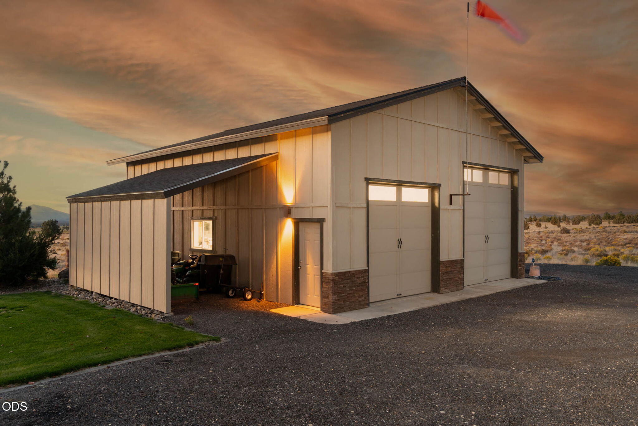 Detached workshop with two large garage doors and an open equipment bay at sunset.