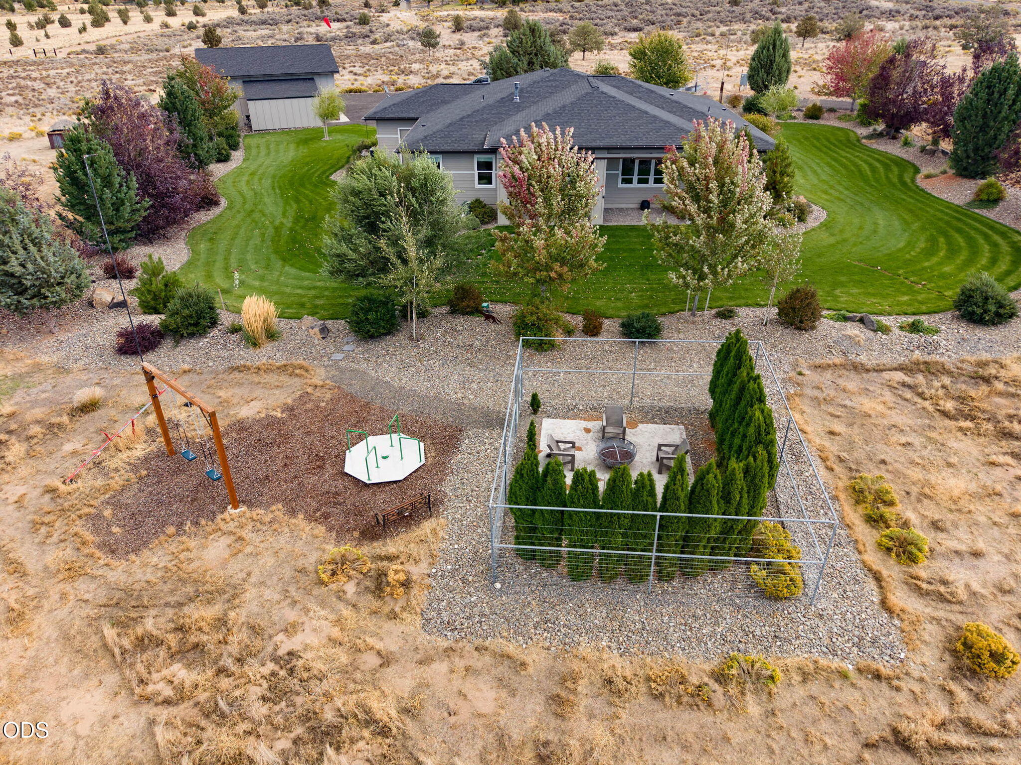 Aerial view of a home with a large lawn, fenced fire-pit patio, and backyard play area.