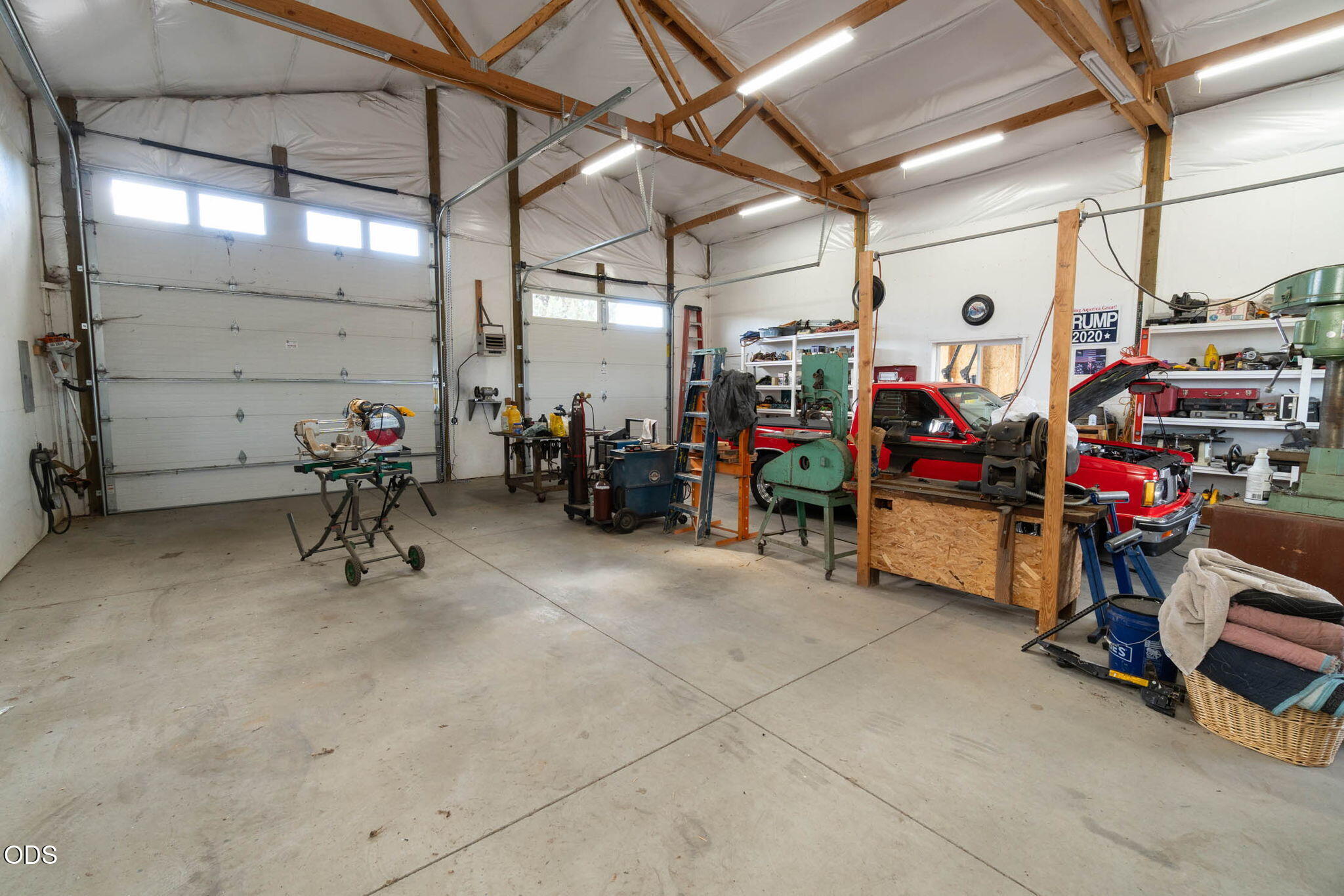 Large workshop with overhead garage doors, woodworking equipment, tool benches, and a red pickup truck.