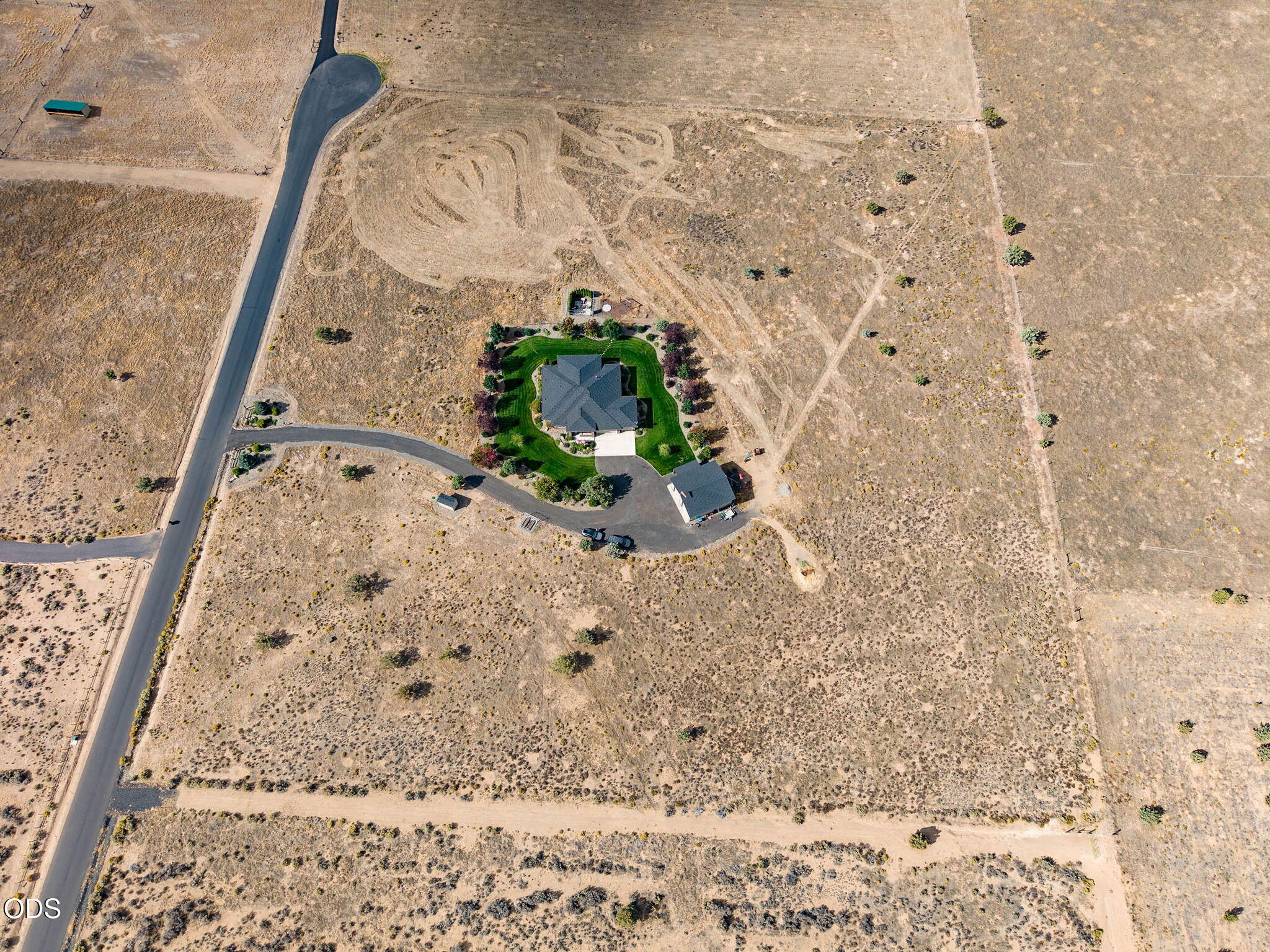 Aerial view of a rural home with a curved driveway, detached outbuilding, and broad open acreage.
