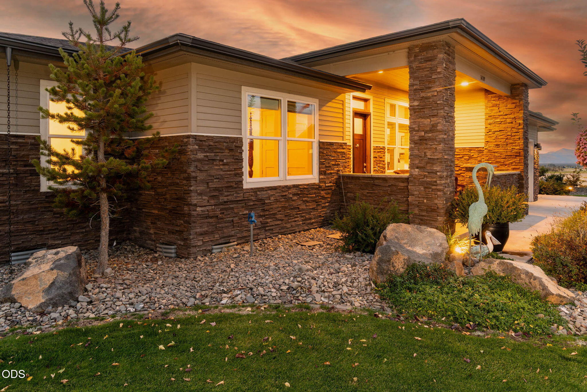 Modern home exterior with stone facade, covered entry, and landscaped rock garden at sunset.