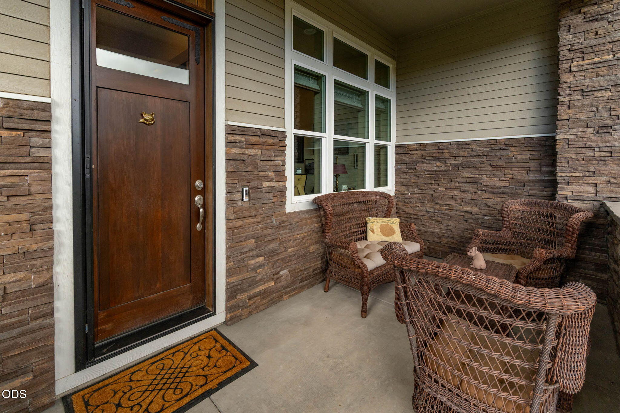 Covered entry porch with a dark wood door, stacked-stone walls, and wicker seating.