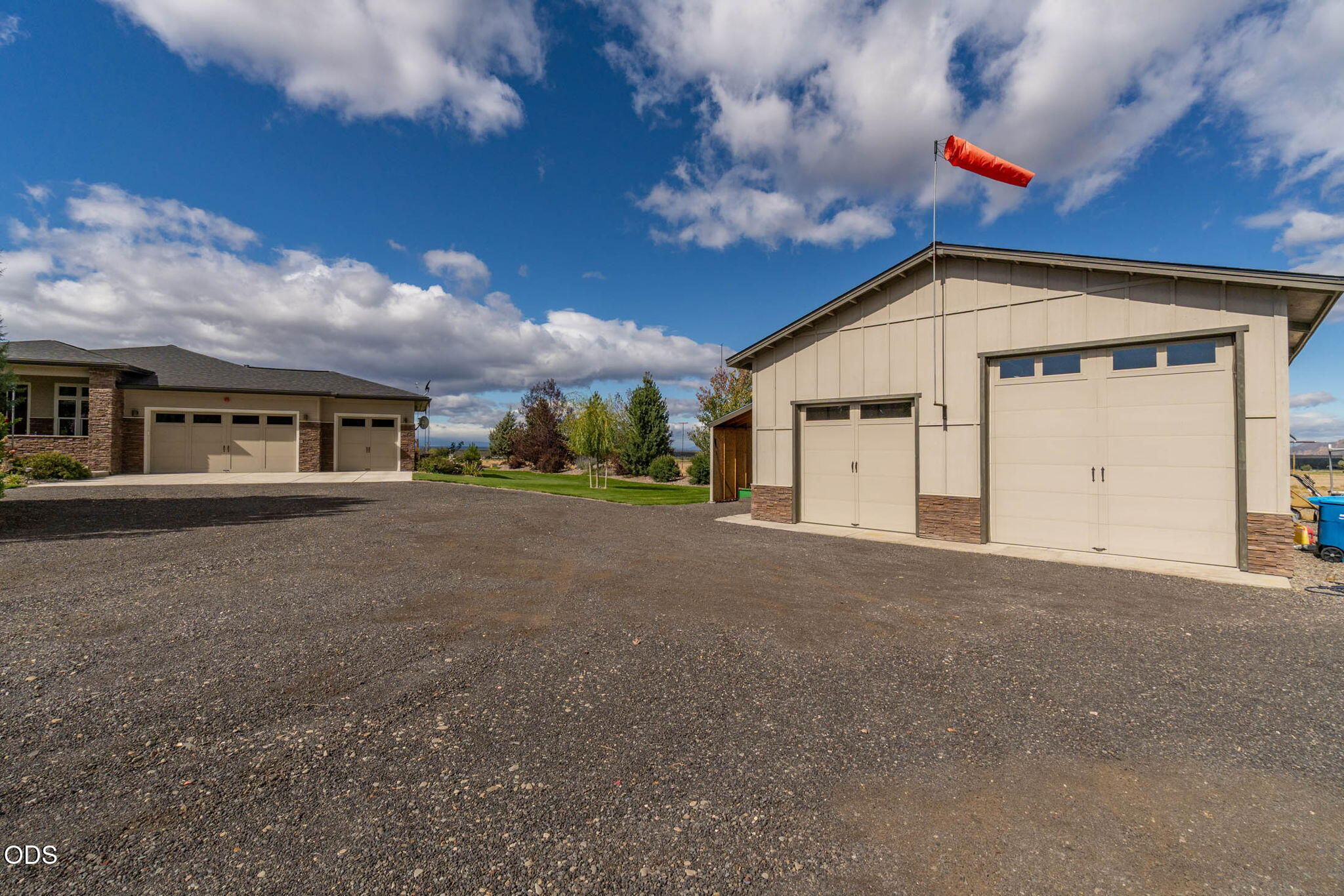 Detached workshop with two garage doors beside the home and a wide gravel driveway.