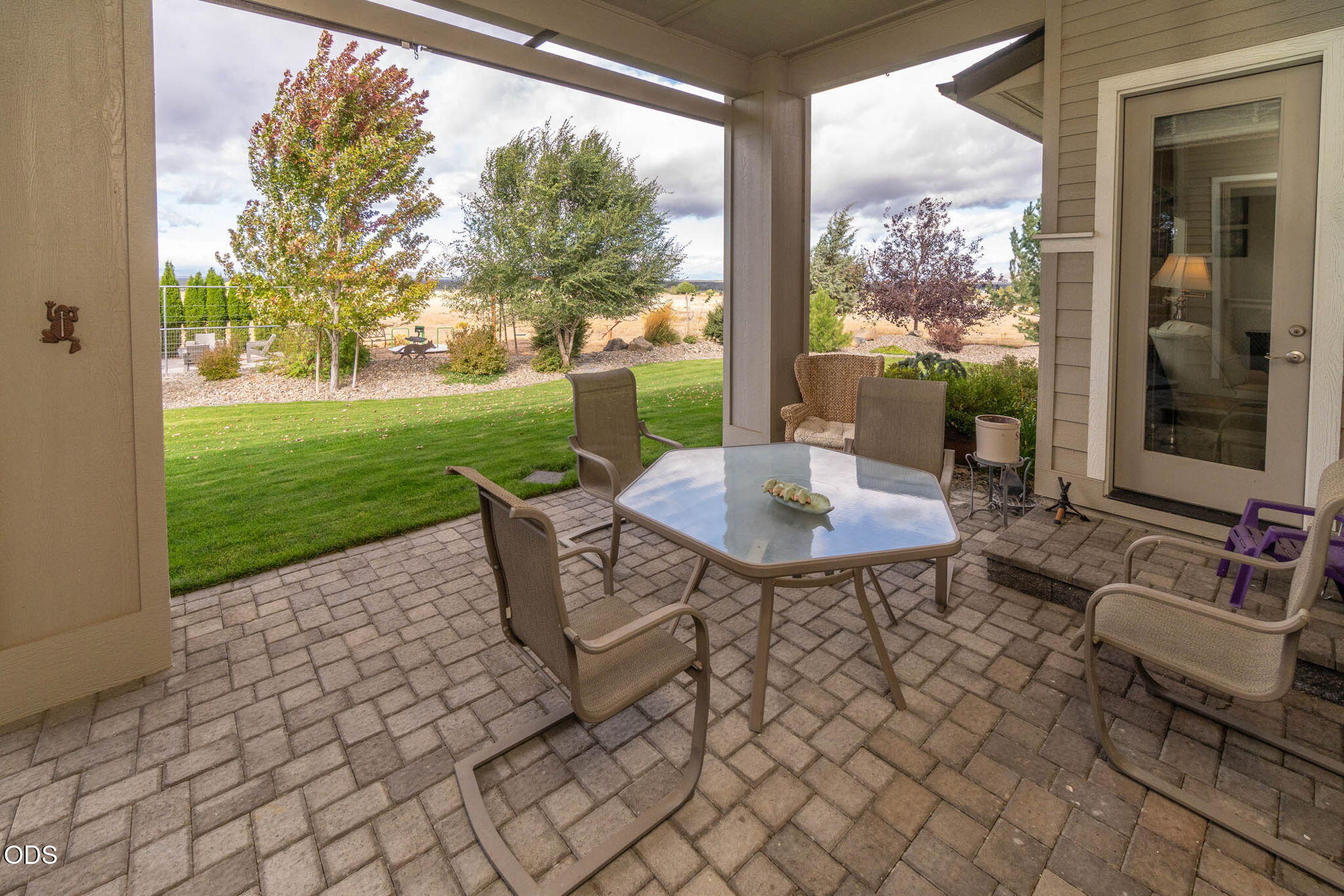 Covered patio with outdoor dining set overlooking a green lawn and landscaped yard.