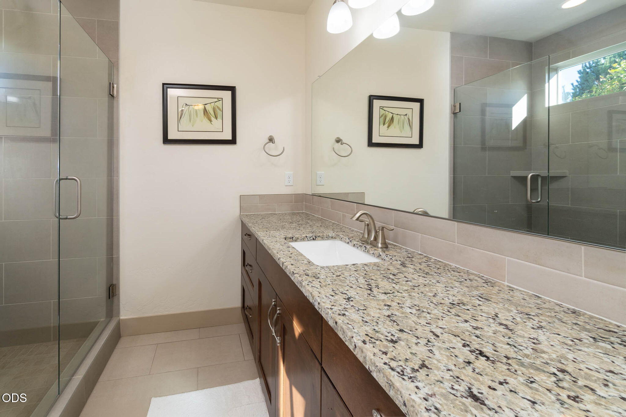 Bathroom with a granite vanity and dark wood cabinets beside a glass-enclosed tile shower.