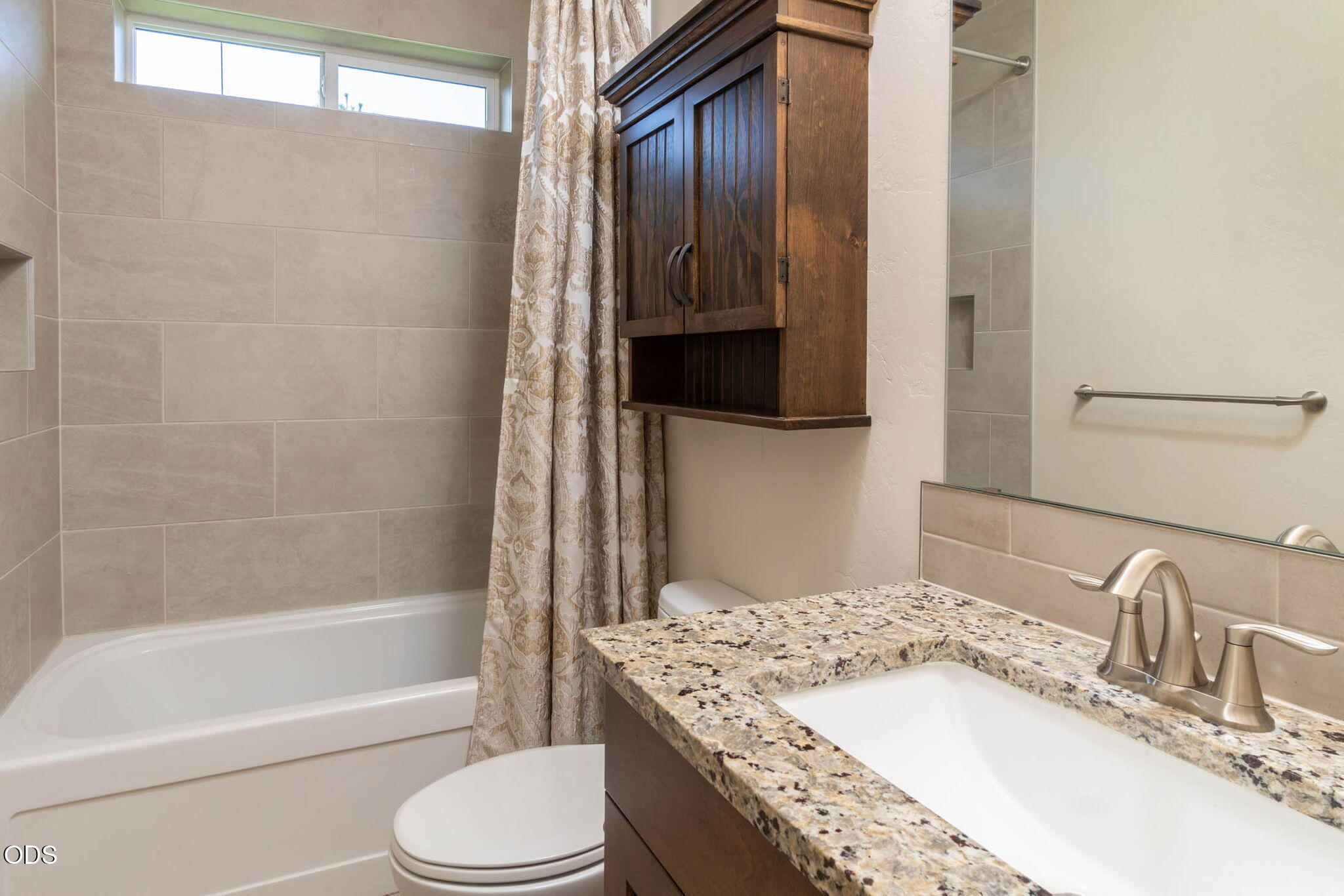 Bathroom with a granite vanity, dark wood cabinet, and tiled bathtub surround.