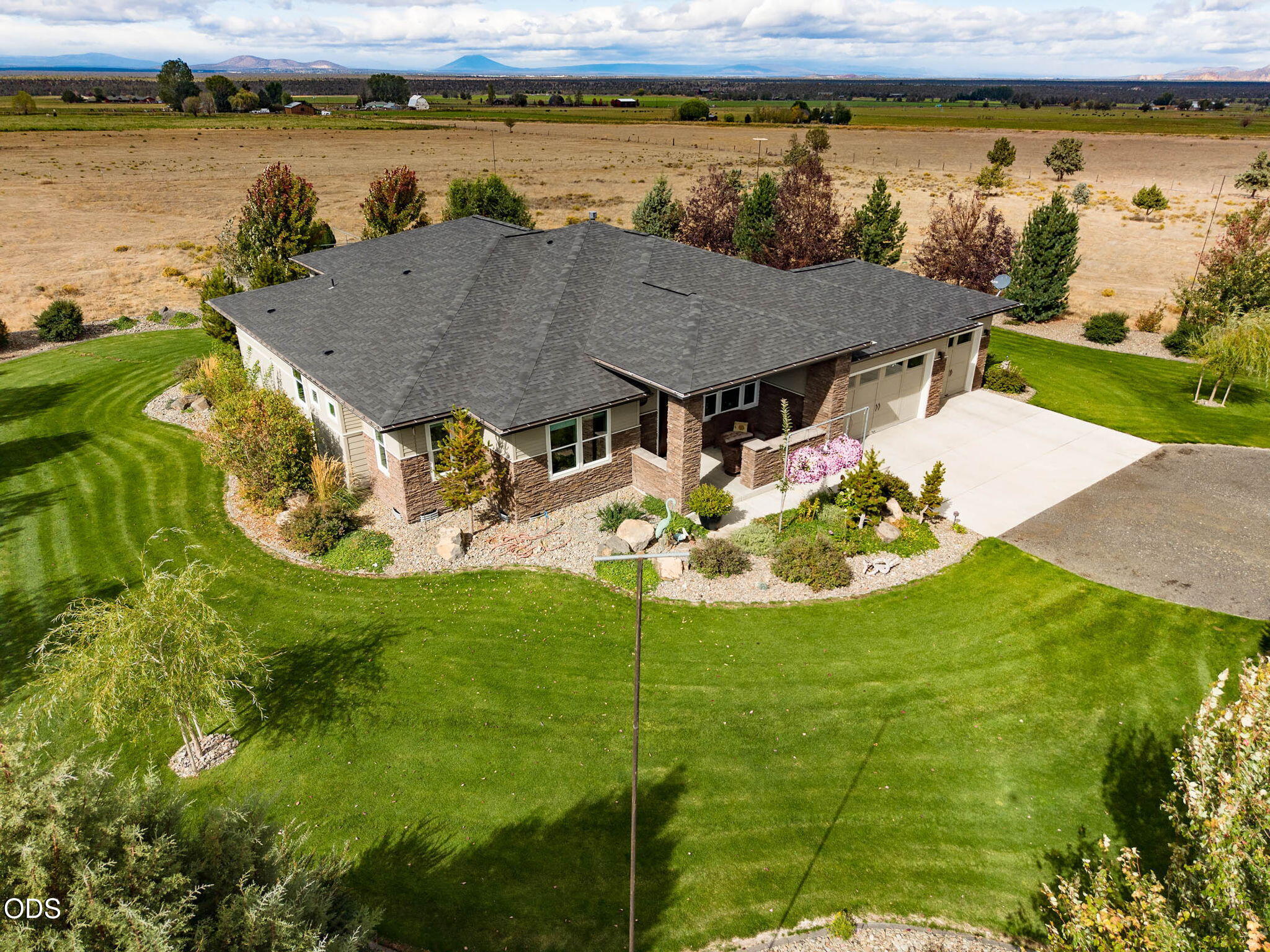 Aerial view of a stone-accented home with a broad green lawn and distant mountain views.