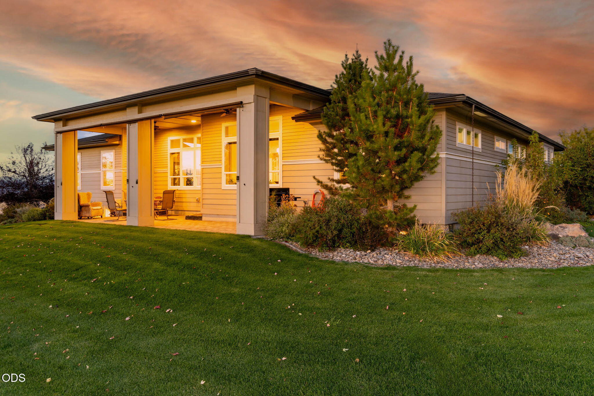 Modern single-story home with a covered patio and landscaped lawn at sunset.