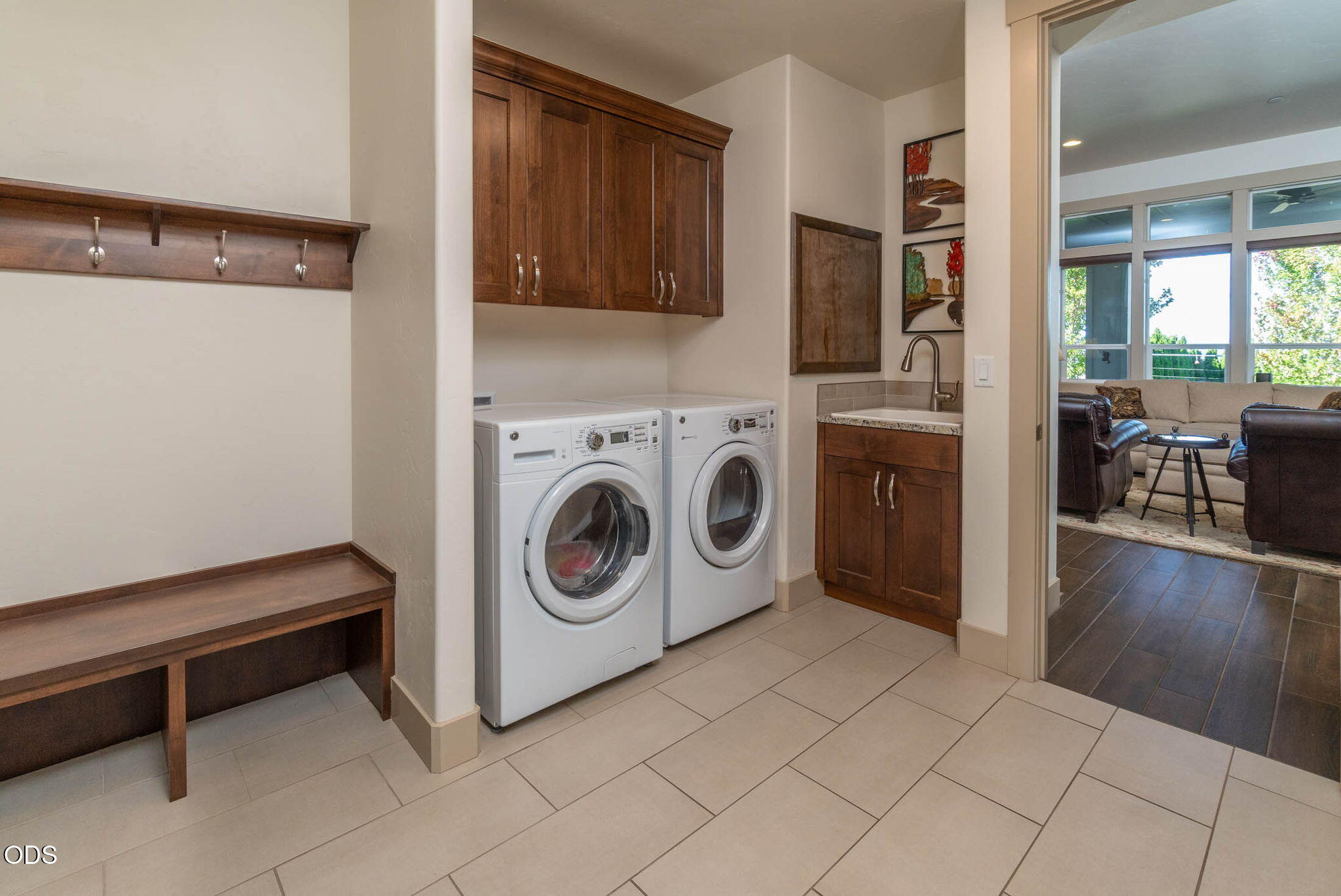 Laundry room with front-loading washer and dryer, dark wood cabinets, utility sink, and built-in bench.