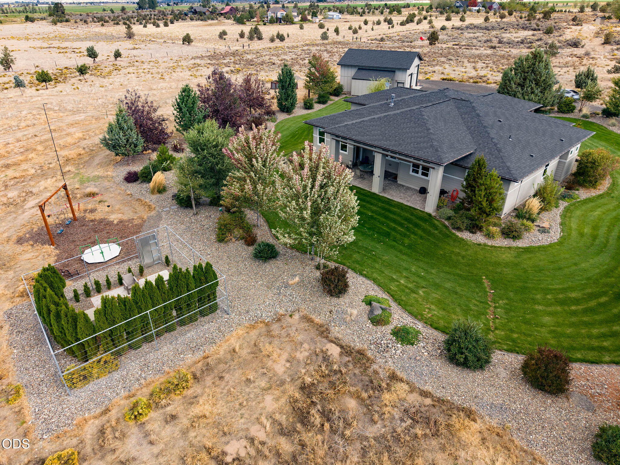 Aerial view of a home with a covered patio, curved lawn, fenced garden, and play area.