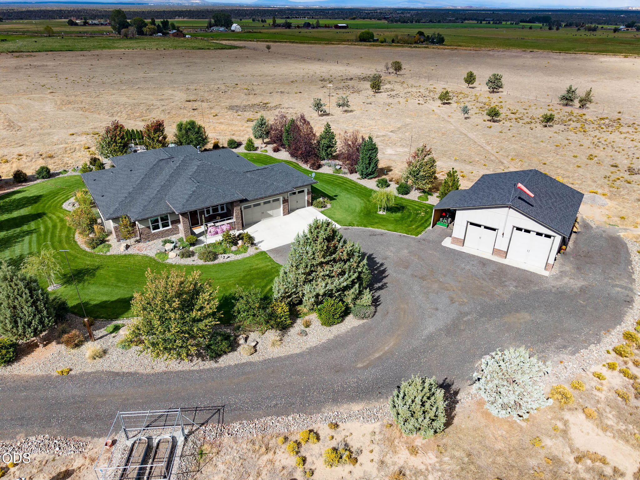 Aerial view of a home, detached garage, landscaped lawn, and surrounding rural acreage.