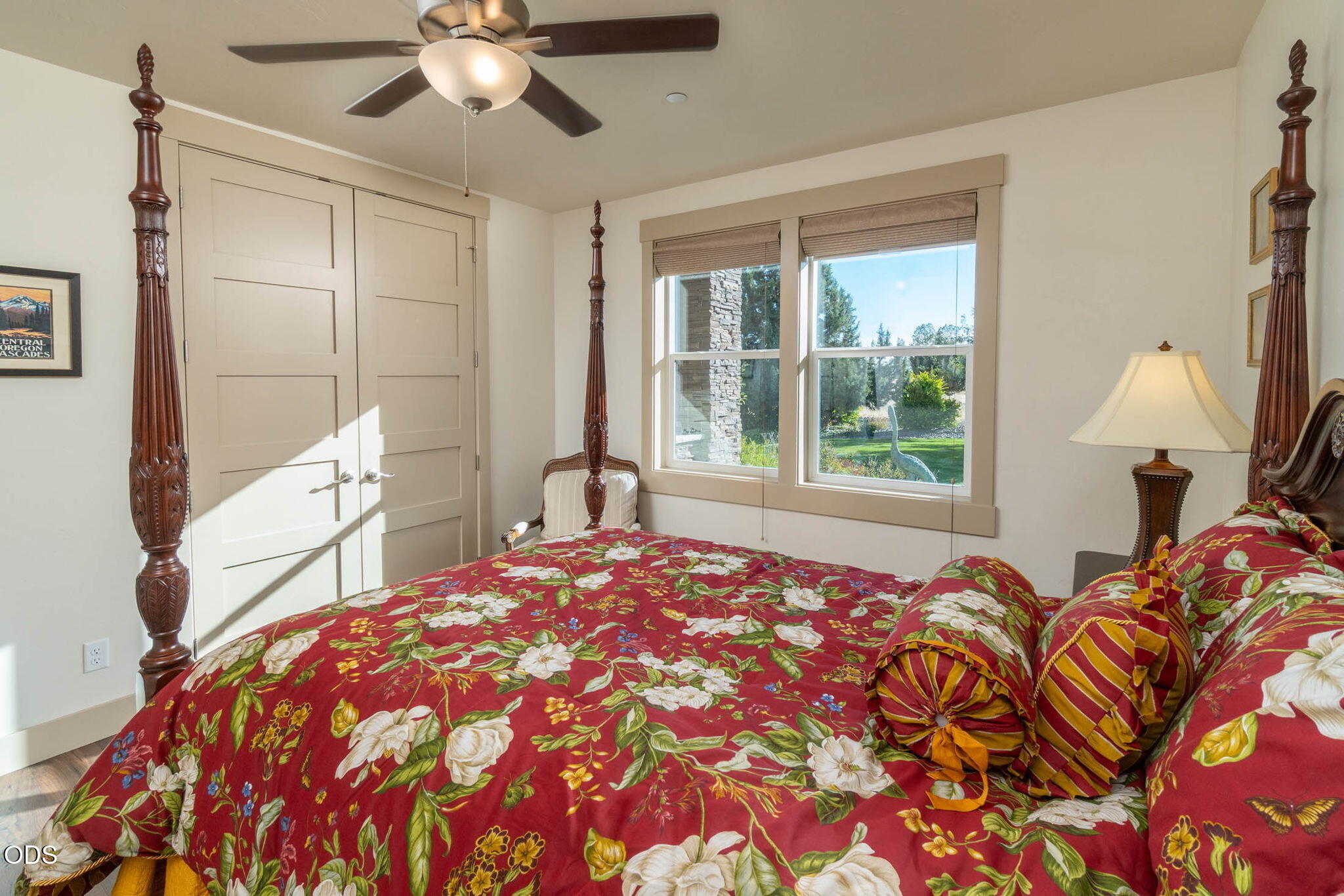 Bedroom with an ornate four-poster bed, red floral bedding, and windows overlooking a garden.