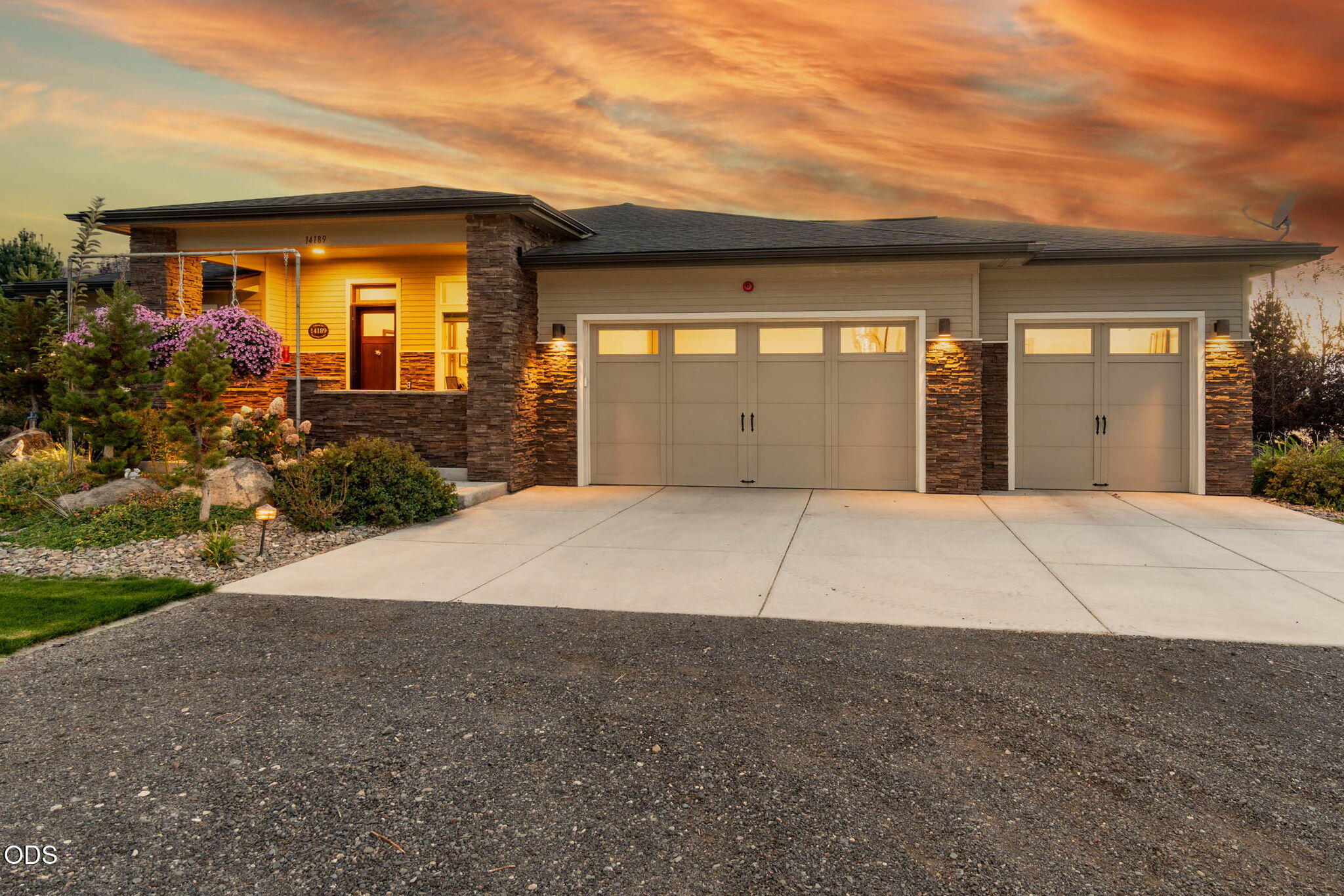 Home exterior at dusk with two garage doors, stone accents, and illuminated landscaping.