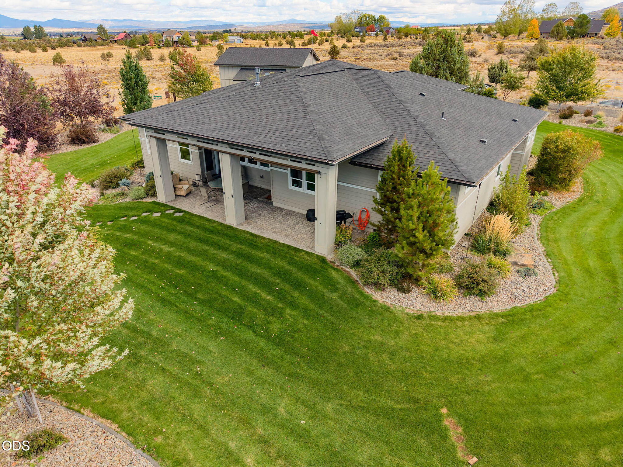 Aerial view of a home with a covered patio, expansive lawn, and autumn landscaping.