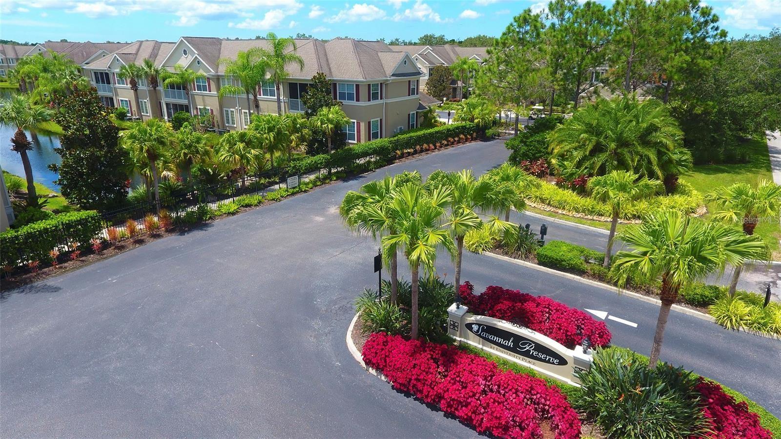 Aerial view of Savannah Preserve entrance, landscaped with palms and bright pink flowers beside rows of attached homes.