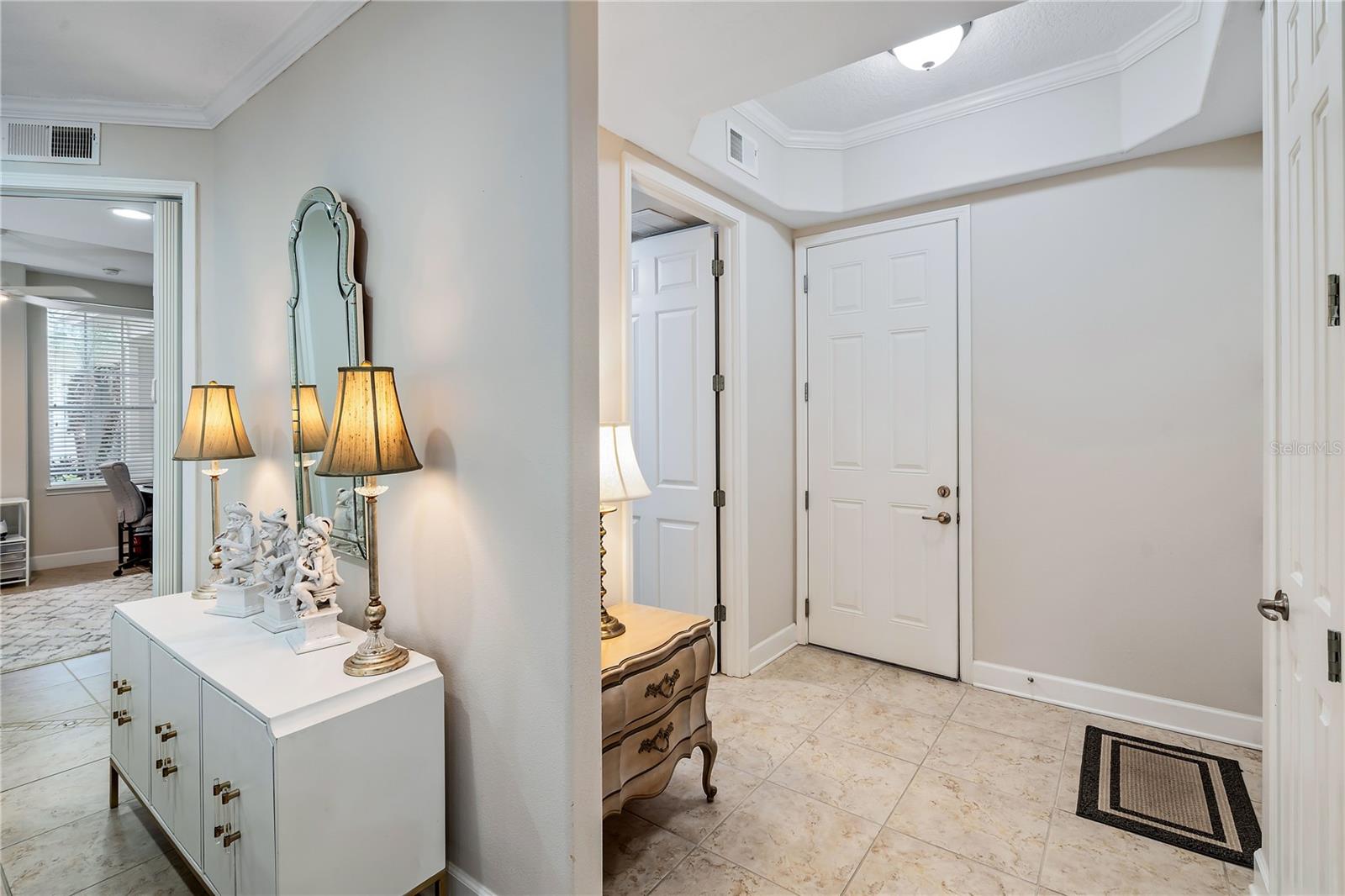 Entry foyer with tiled floors, a white console, lamps, and a tall mirror beside the front door.