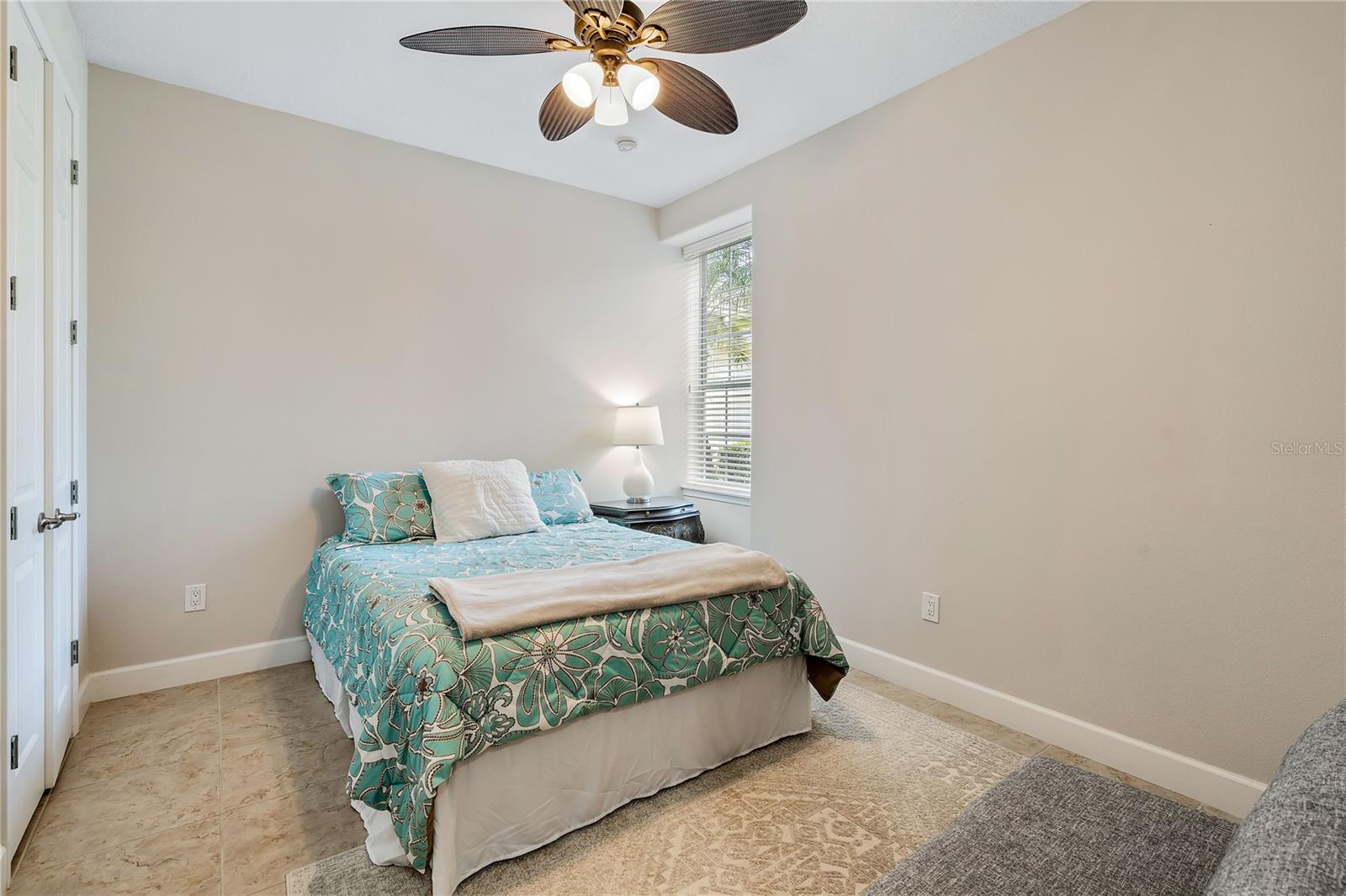 Bedroom with turquoise floral bedding, a window with blinds, and a ceiling fan.