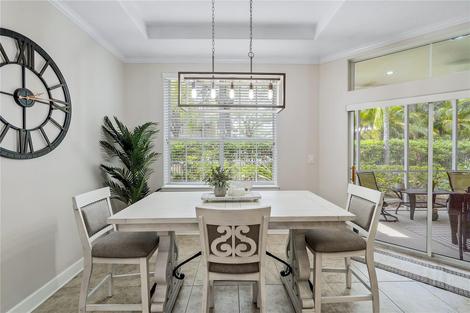 Dining room with a white table, rectangular pendant light, oversized wall clock, and sliding doors to a patio.