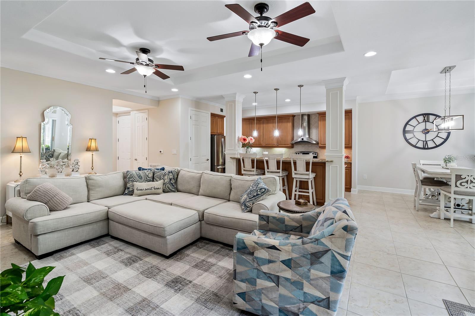 Open-plan living room with a large sectional, patterned armchair, and wood-cabinet kitchen behind it.