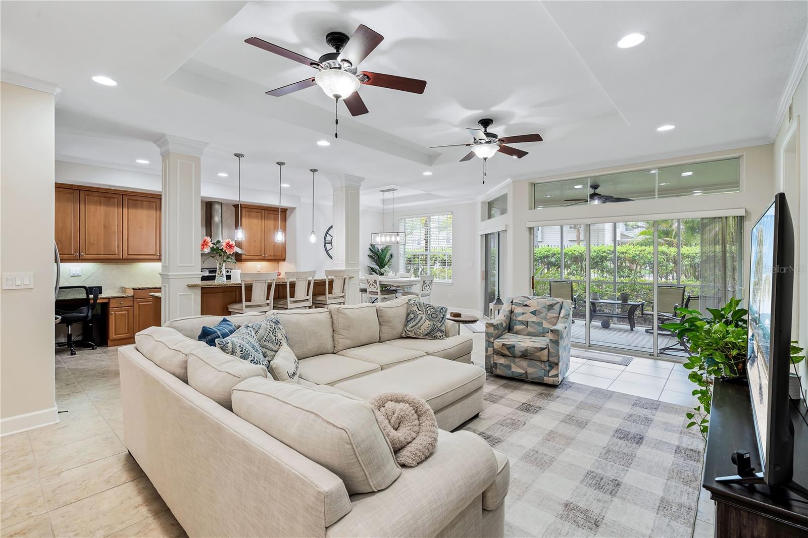 Open-plan living room with a large cream sectional, adjoining wood-cabinet kitchen, and sliding doors to a screened patio.