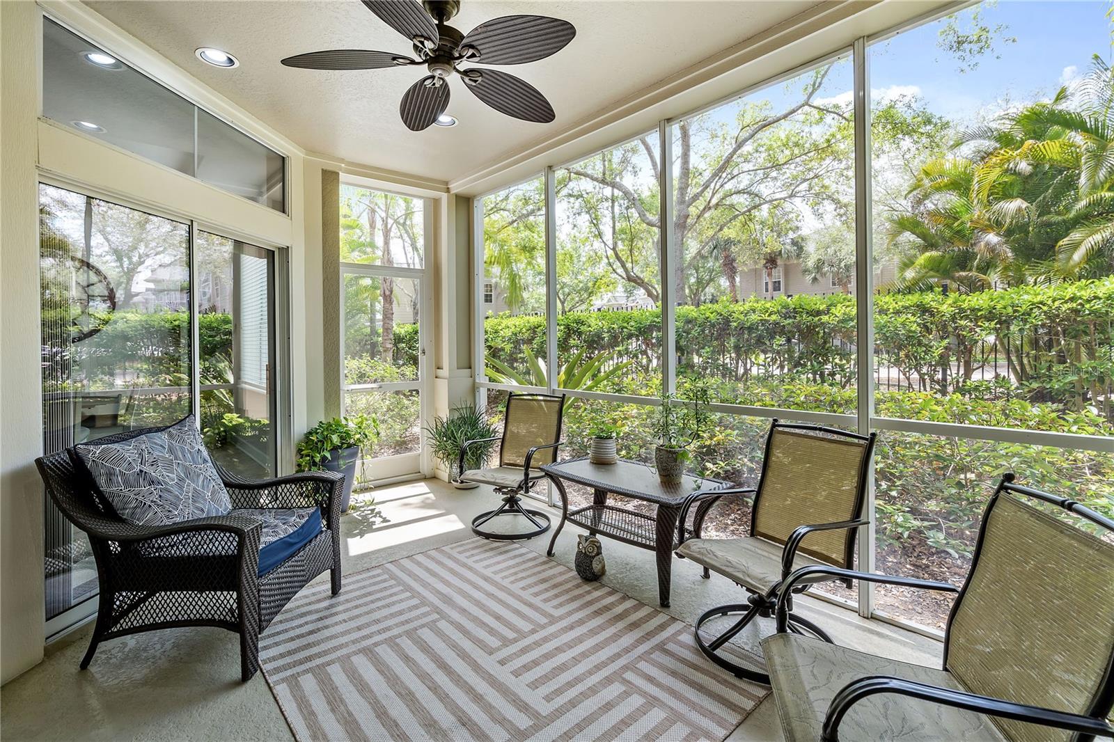 Screened patio with wicker seating, a ceiling fan, and views of tropical landscaping.