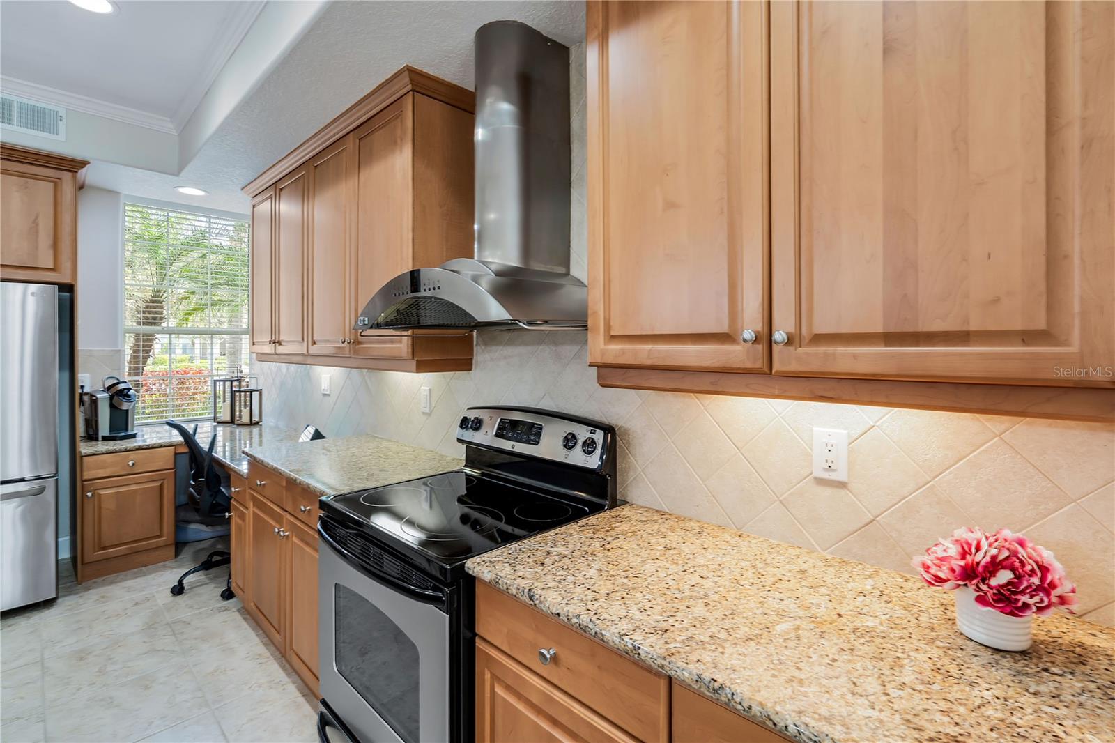 Kitchen with warm wood cabinets, granite counters, and a black electric range beneath a stainless-steel hood.