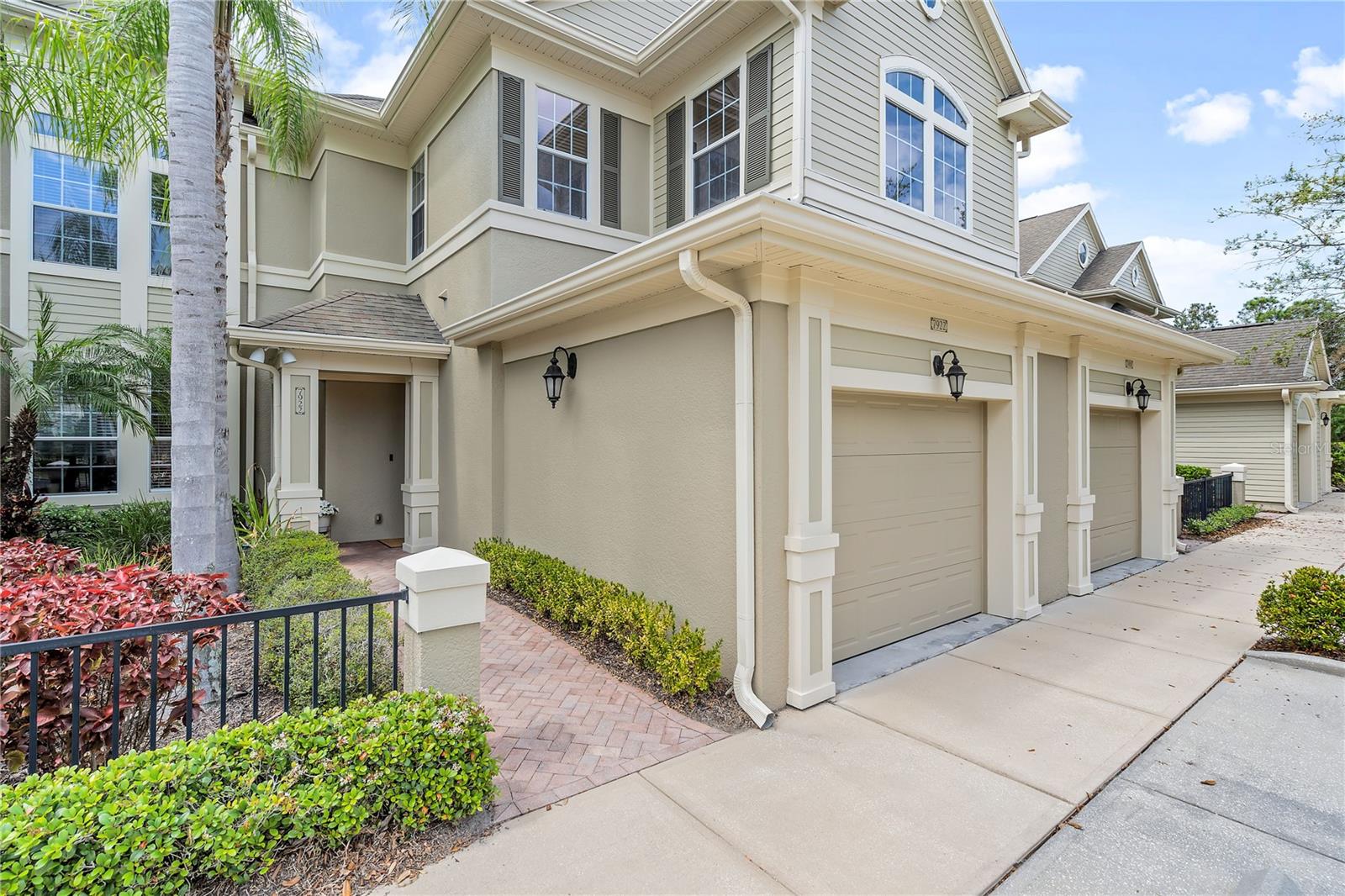 Two-story beige townhouse with arched windows, attached garages, and a landscaped brick walkway.