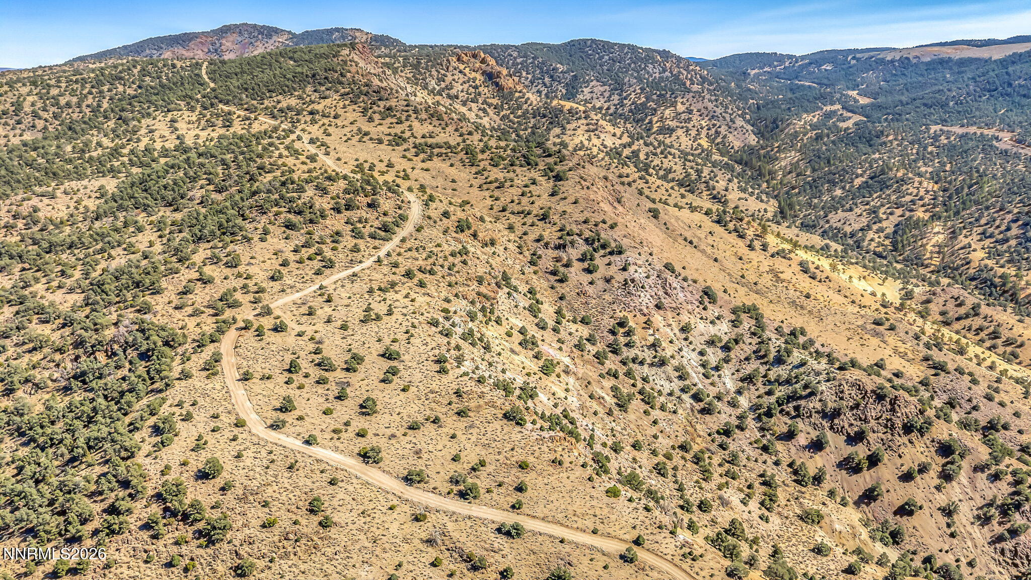 Aerial view of rugged vacant land with a winding dirt road crossing shrub-covered hills.