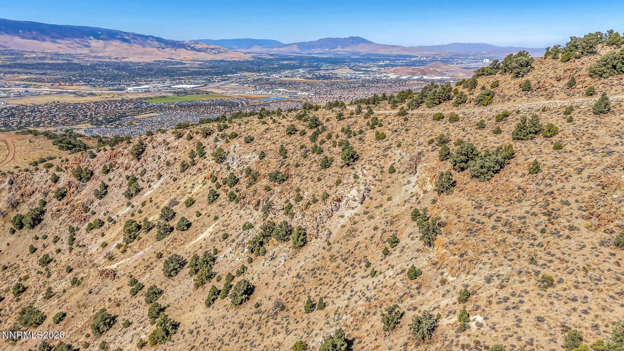 Rocky hillside overlooking Reno, with the city and distant mountain ranges in the background.