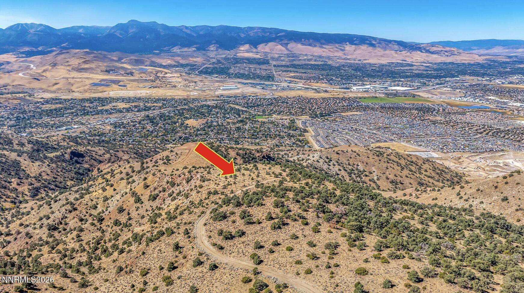 Aerial view of a hillside parcel marked by an arrow, overlooking Reno and surrounding mountains.