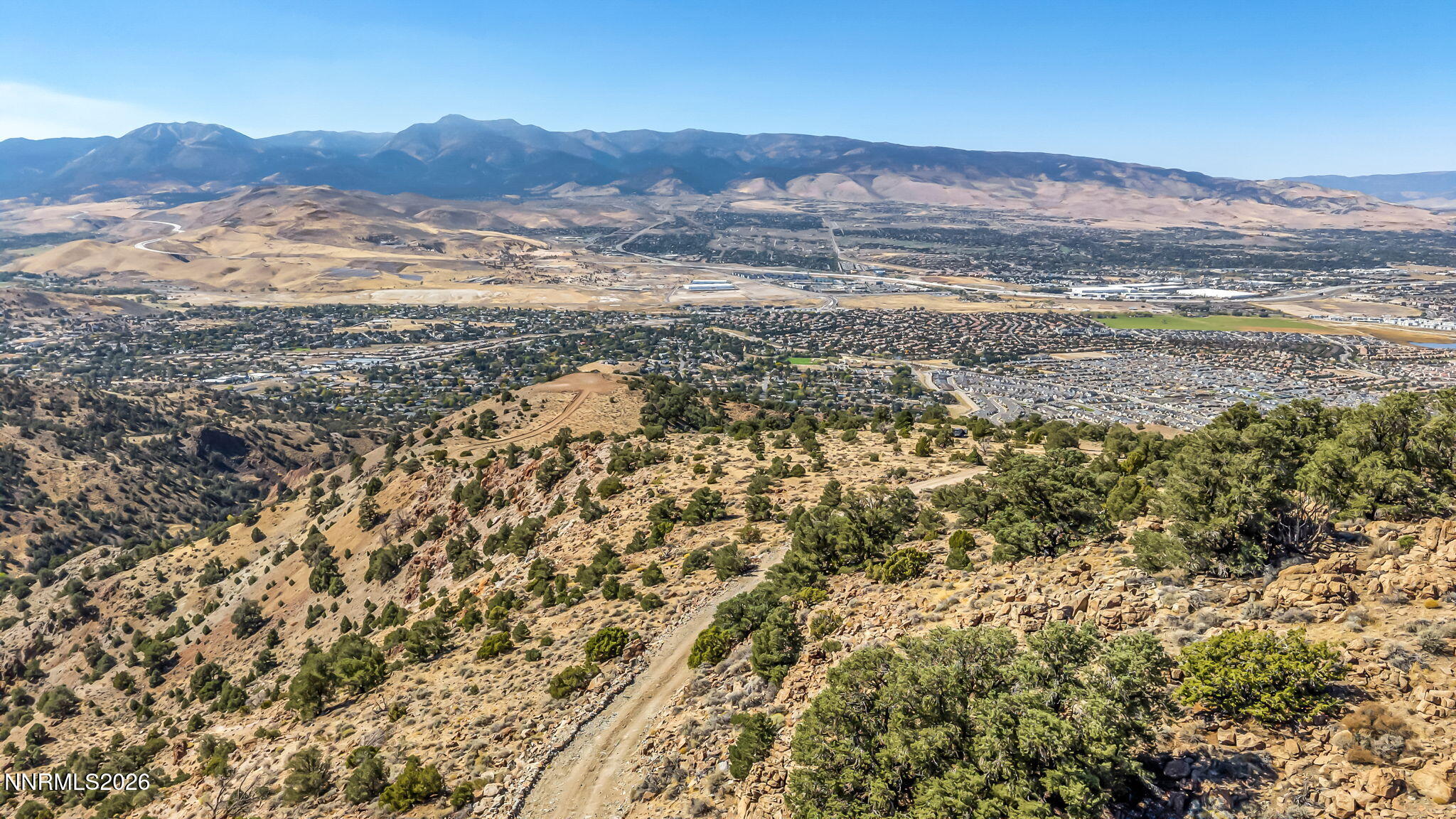 Panoramic view of the Reno valley from a rocky hillside, with neighborhoods and mountains beyond.