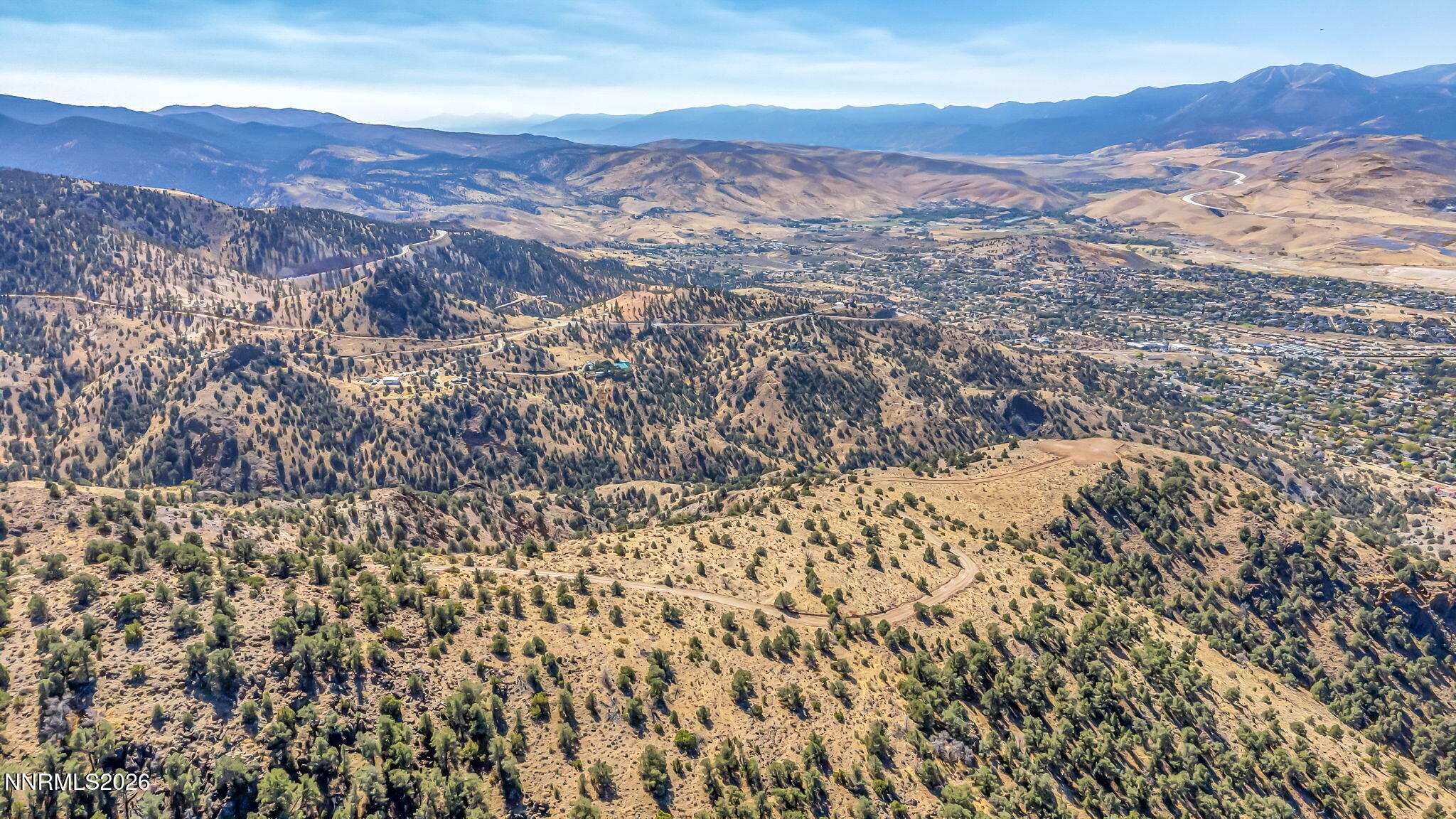 Aerial view of rugged Nevada hills, winding roads, valley development, and distant mountains.