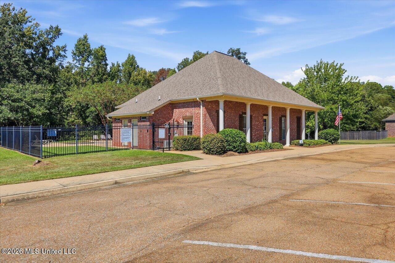 Brick building with a broad hipped roof, white columns, and fenced side yard.