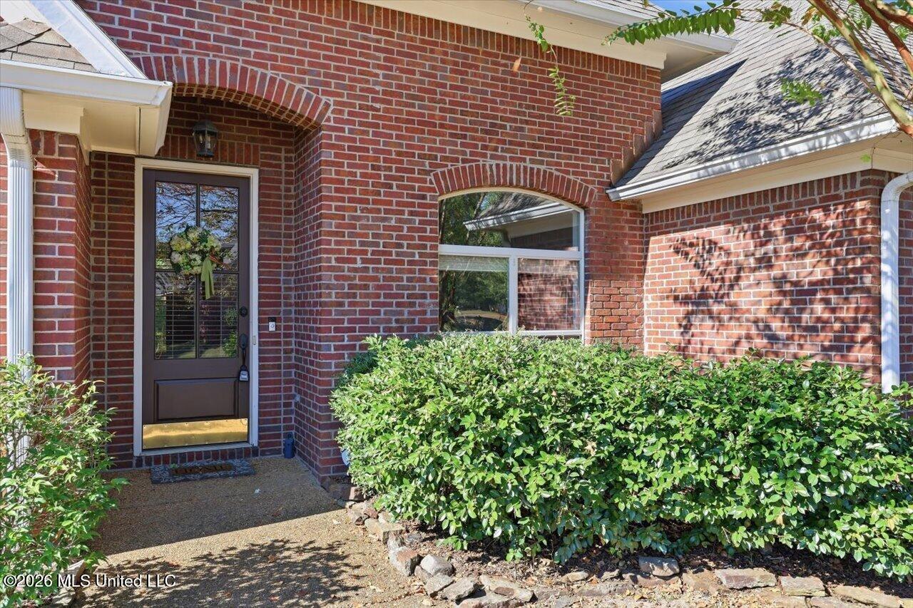 Brick home entrance with an arched doorway, glass door, and front hedges.